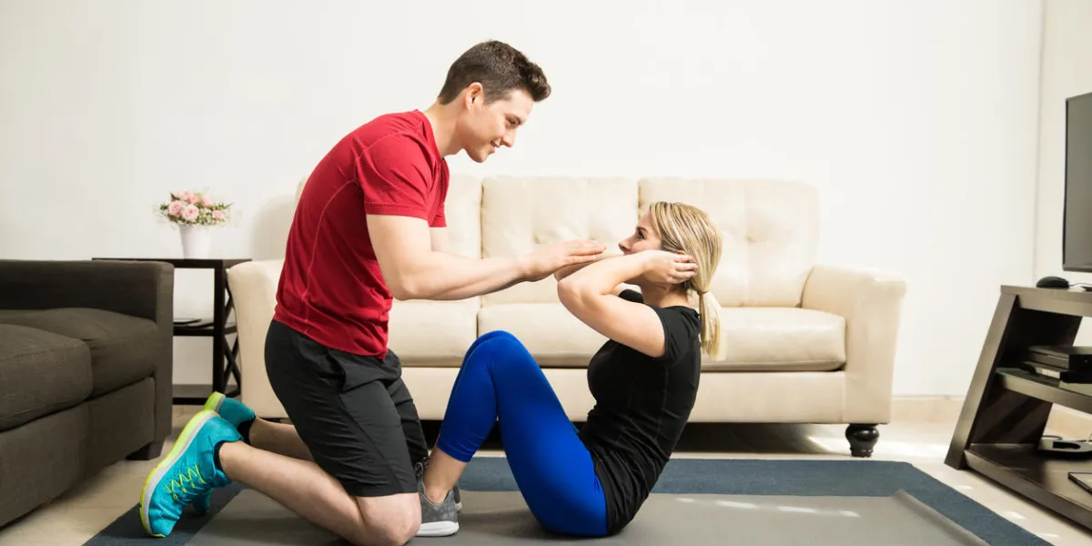 profile view of a young latin couple doing some crunches together and helping each other out