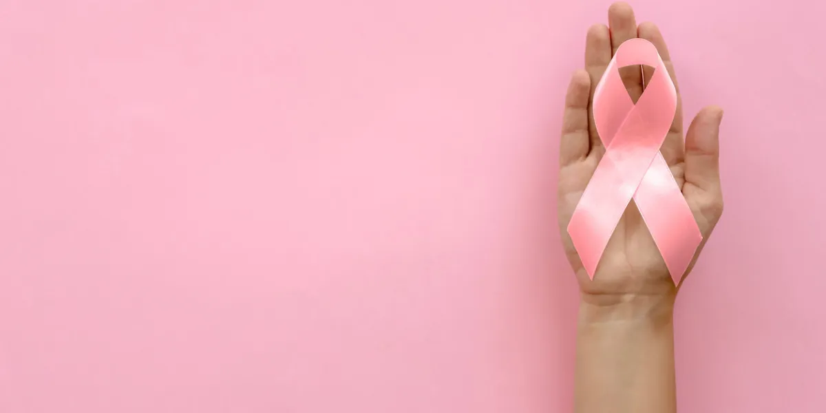 woman holding symbolic ribbon of breast cancer awareness on color background, top view gynecological care