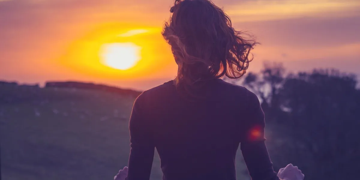 rear view of young woman admiring the sunset over a field from her balcony