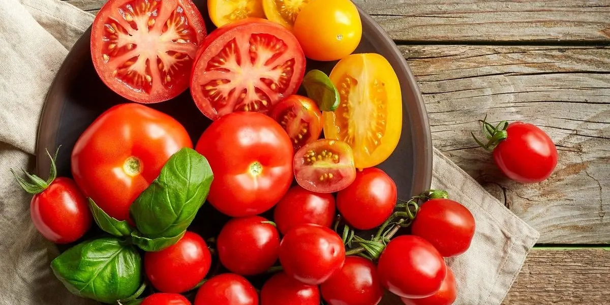 plate of various colorful tomatoes on wooden kitchen table, top view