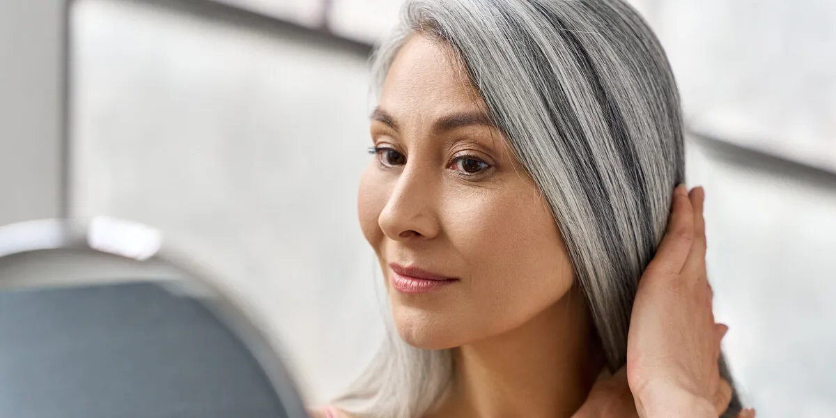 portrait of beautyful happy middle aged mature asian woman, senior older 50s lady pampering touching gray hair looking at herself at mirror indoors ads of lifting anti wrinkle skin hair care spa portrait of beautyful happy middle aged mature asian woman, senior older 50s lady pampering touching gray hair looking at herself at mirror indoors ads of lifting anti wrinkle skin hair care spa