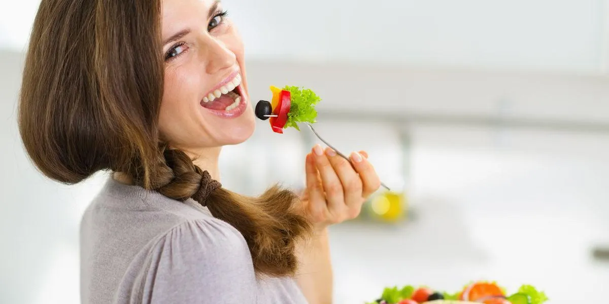 souriante jeune femme mangeant une salade fraîche dans la cuisine moderne