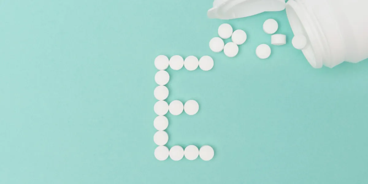 vitamin e pills forming the letter 'e' with toppled medicine bottle over turquoise background vitamin e pills forming the letter 'e' with toppled medicine bottle over turquoise background