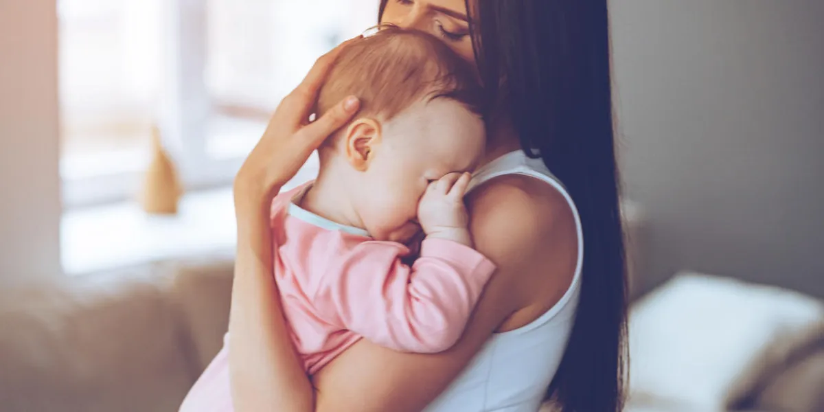 side view of beautiful young woman holding sleepy baby girl in her arms and bonding with her while standing at home side view of beautiful young woman holding sleepy baby girl in her arms and bonding with her while standing at home