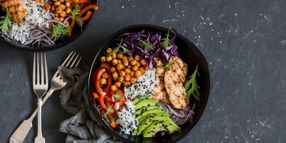 grilled chicken, rice, spicy chickpeas, avocado, cabbage, pepper buddha bowl on dark background, top view delicious balanced food concept