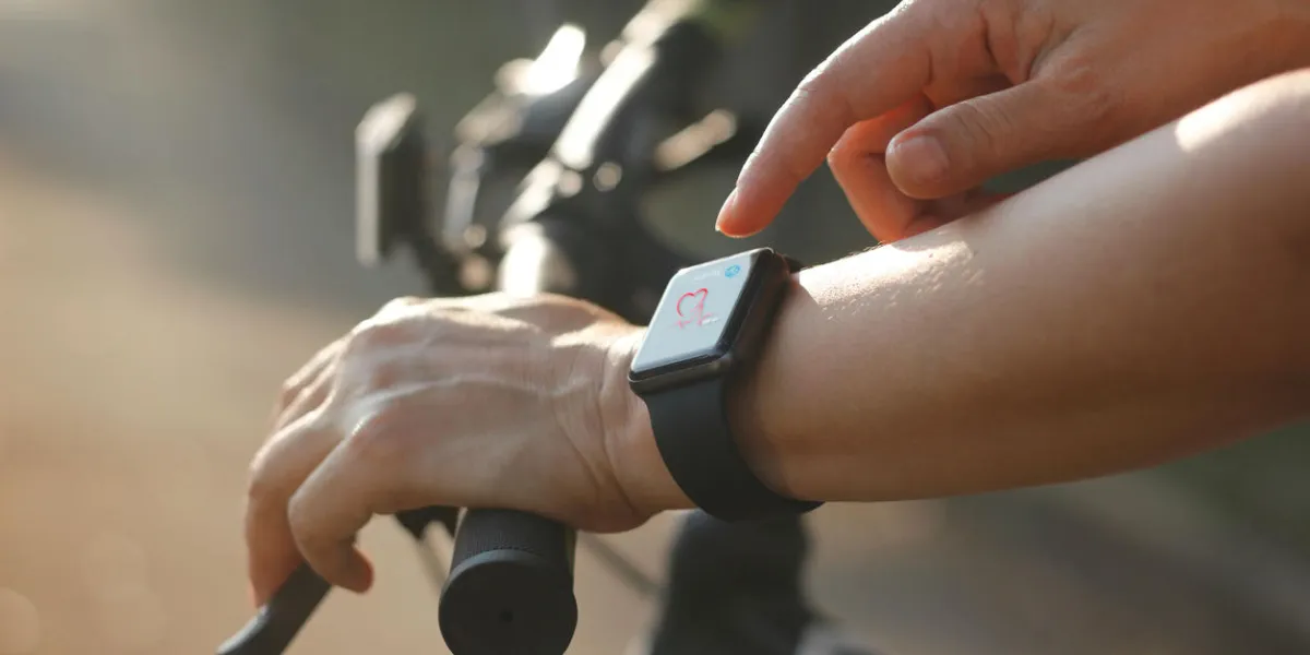 woman cyclist hands with heart rate icon on smart watch, bicycle at summer trail all on screen are design up