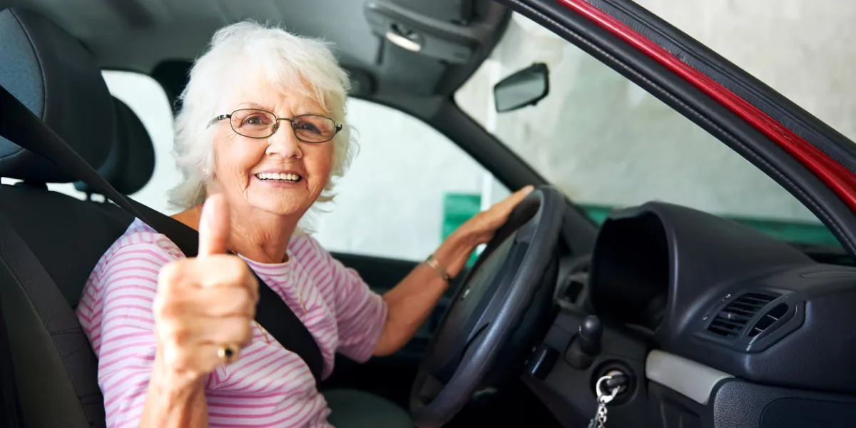 une femme âgée positive assis dans une voiture montrant un coup de pouce