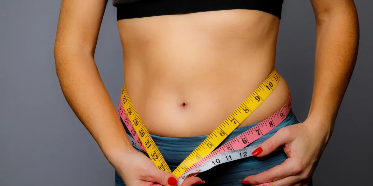 woman in active wear with squeezed measuring tape on a gray background