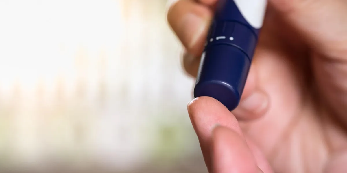 medicine, diabetes, glycemia, health care and people concept - close up of man hands using lancet on finger to check blood sugar level by glucose meter