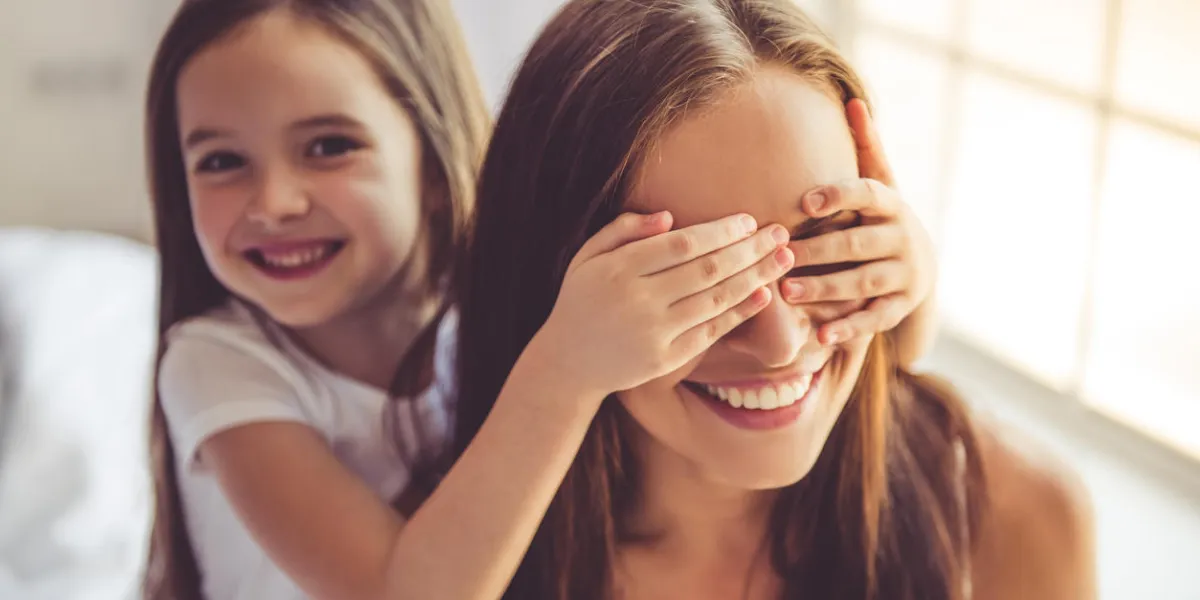 beautiful young woman and her charming little daughter are hugging, looking at camera and smiling