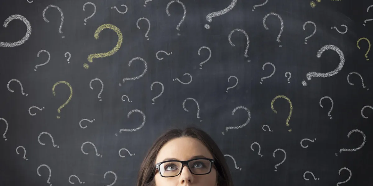 businesswoman's head is visible surrounded by question marks drawn on a blackboard behind her the woman is facing the viewer, and her eyes look up