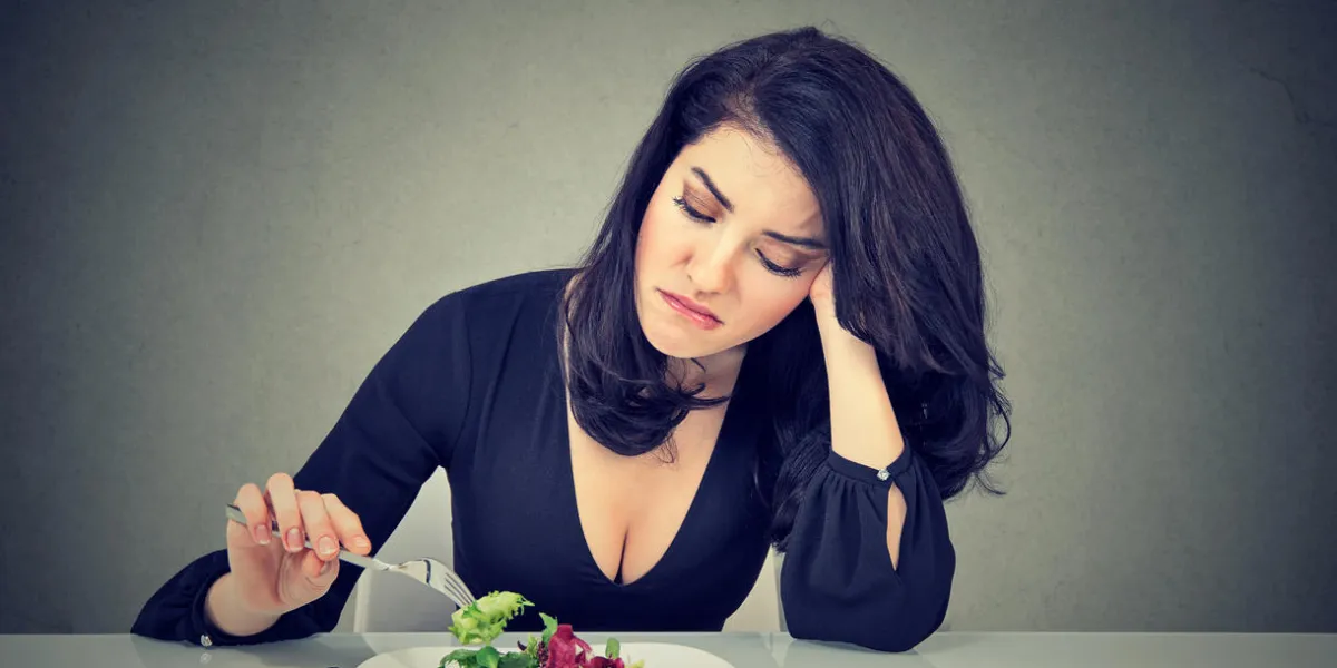 displeased young woman eating green leaf lettuce tired of diet restrictions