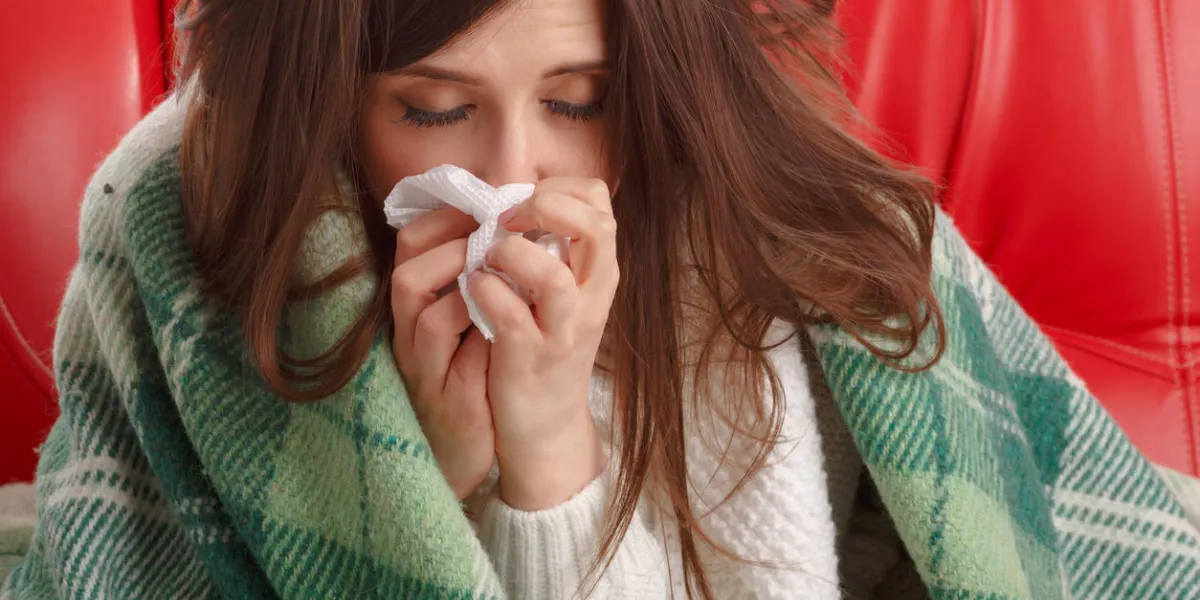 sick young woman sitting on a red couch, and blowing his nose into a napkin woman sick blowing nose isolated sick woman flu woman caught cold