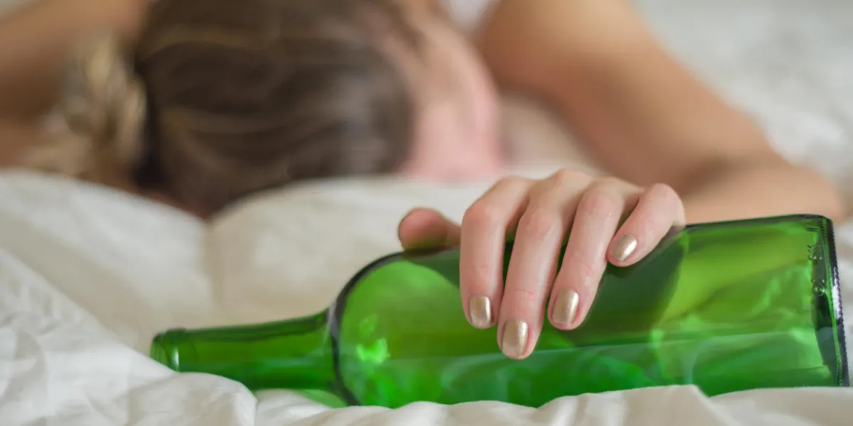 great concept of alcohol abuse young woman, blond hair, fainted in bed after drinking too much alcohol glass of wine in hand, bottle of wine