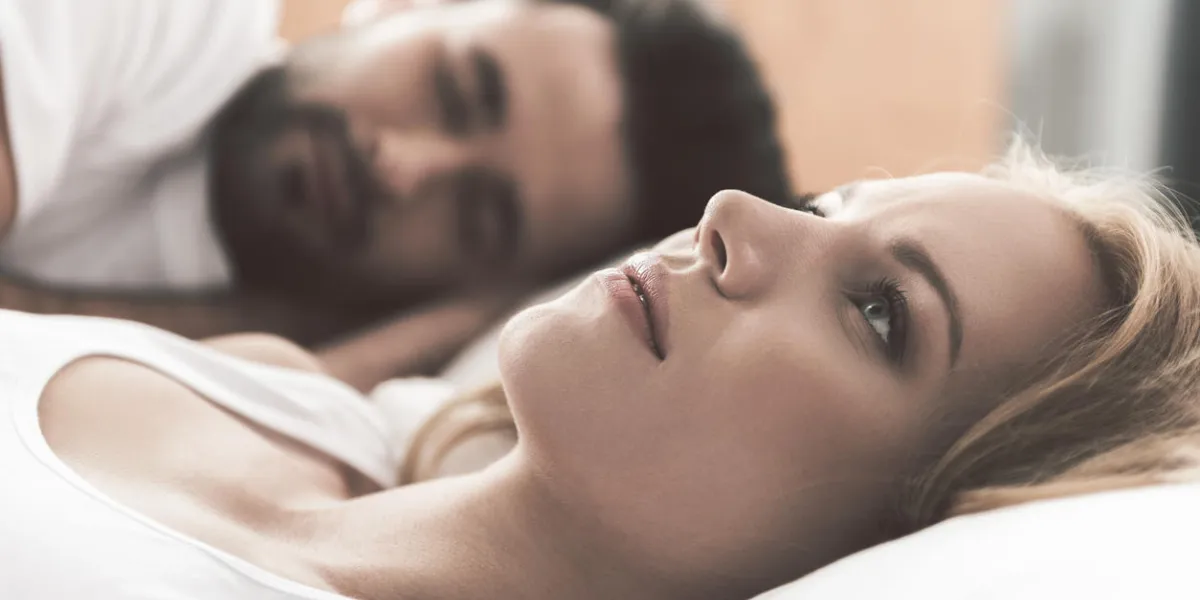 nervous young woman is lying on bed and thinking seriously her husband is sleeping on background nervous young woman is lying on bed and thinking seriously her husband is sleeping on background