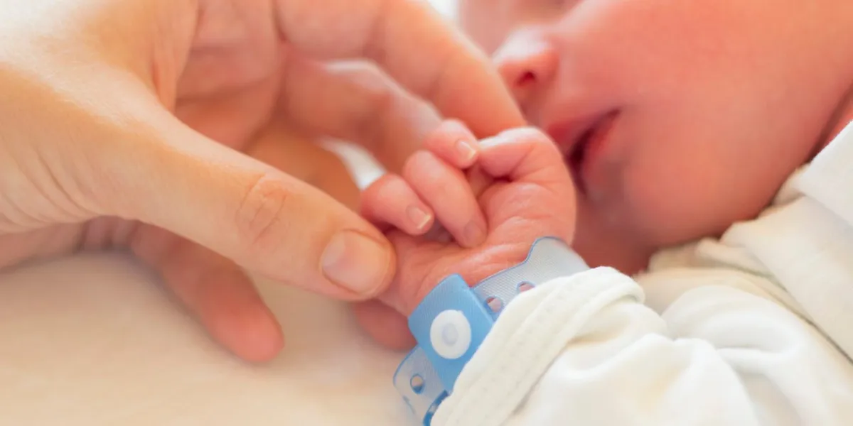 newborn baby boy sleeping in his crib, his mother's hand holding his little hand
