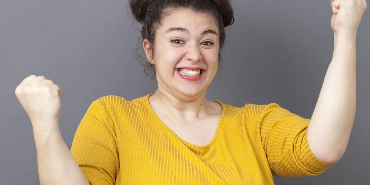 concept de réussite - compétitive jeune grosse fille portant un chandail jaune exprimant sa réalisation et la joie avec les deux poings