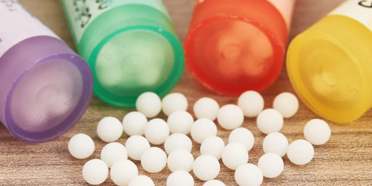 homeopathic globules scattered around with their colored containers in the shape of tube on a wooden table