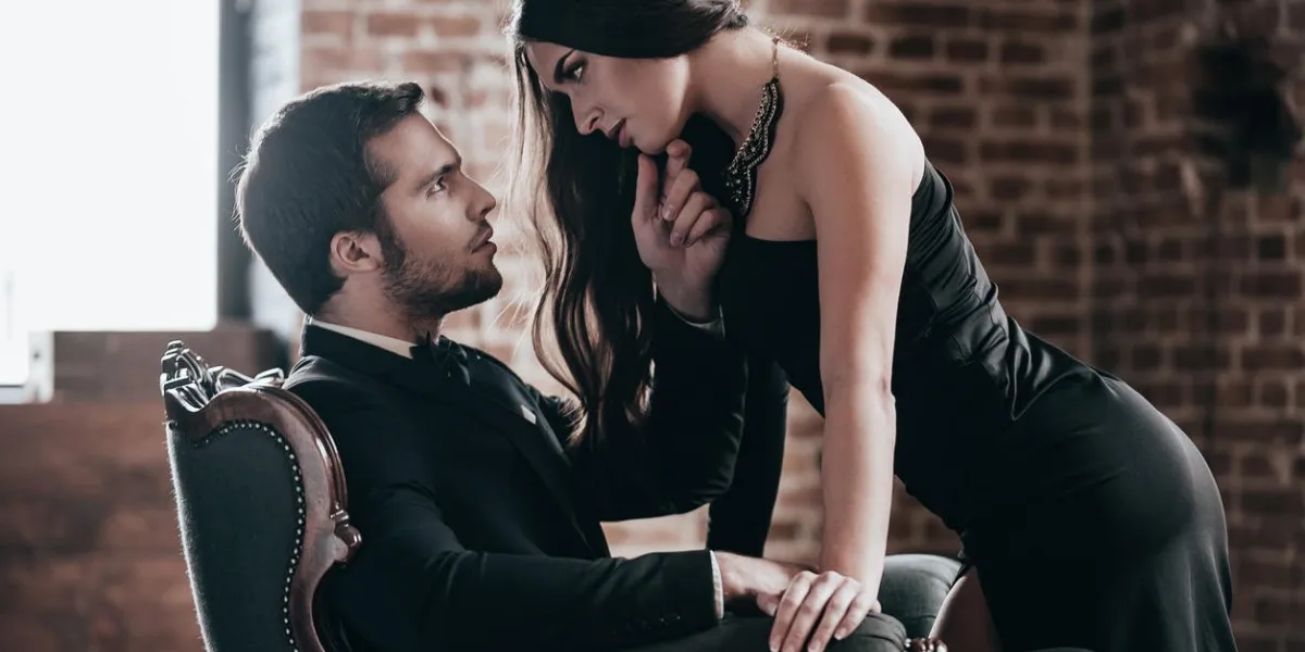 beautiful young woman in cocktail dress leaning to her boyfriend sitting in chair while looking at each other in loft interior beautiful young woman in cocktail dress leaning to her boyfriend sitting in chair while looking at each other in loft interior