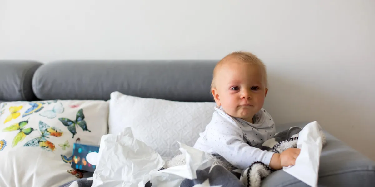 sick little toddler boy, sitting on a couch in living room with a box of tissues
