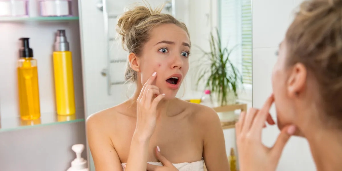 young beautiful woman surprised to see pimple on skin unhappy girl with stunned funny face standing in towel in bathroom, looking in the mirror, pointing to zit young beautiful woman surprised to see pimple on skin unhappy girl with stunned funny face standing in towel in bathroom, looking in the mirror, pointing to zit