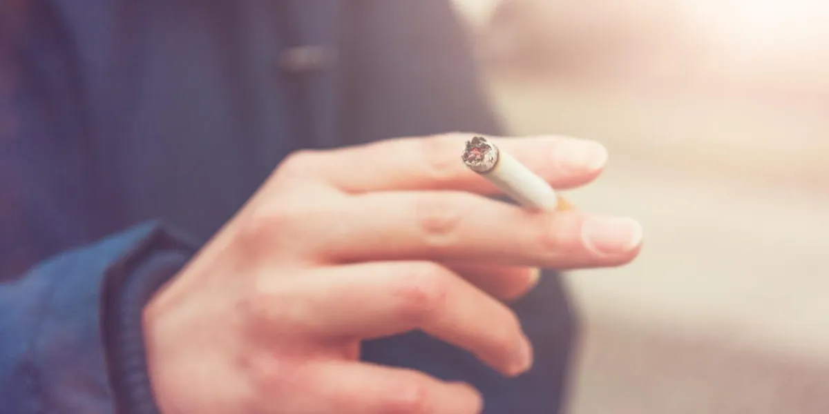 toned image of a woman smoking a cigarette holding it between her fingers, close up view of his hand toned image of a woman smoking a cigarette holding it between her fingers, close up view of his hand
