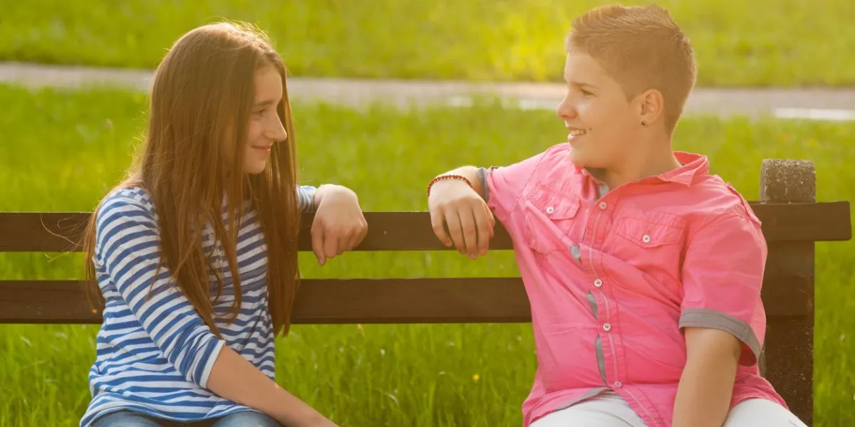 happy boy and a girl sitting on the bench and looking at each other on sunny spring day