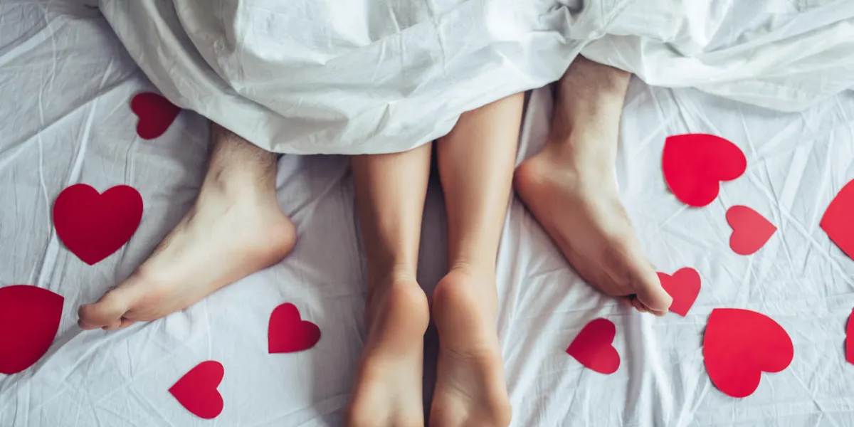 cropped image of young couple is lying on bed close up of male and female feet loving couple is lying on bed under blanket covered by small red paper hearts saint valentines day cropped image of young couple is lying on bed close up of male and female feet loving couple is lying on bed under blanket covered by small red paper hearts saint valentines day