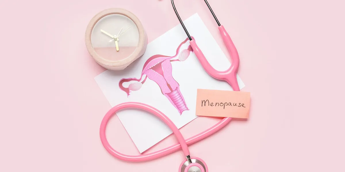 papers with word menopause, uterus, stethoscope and alarm clock on pink background