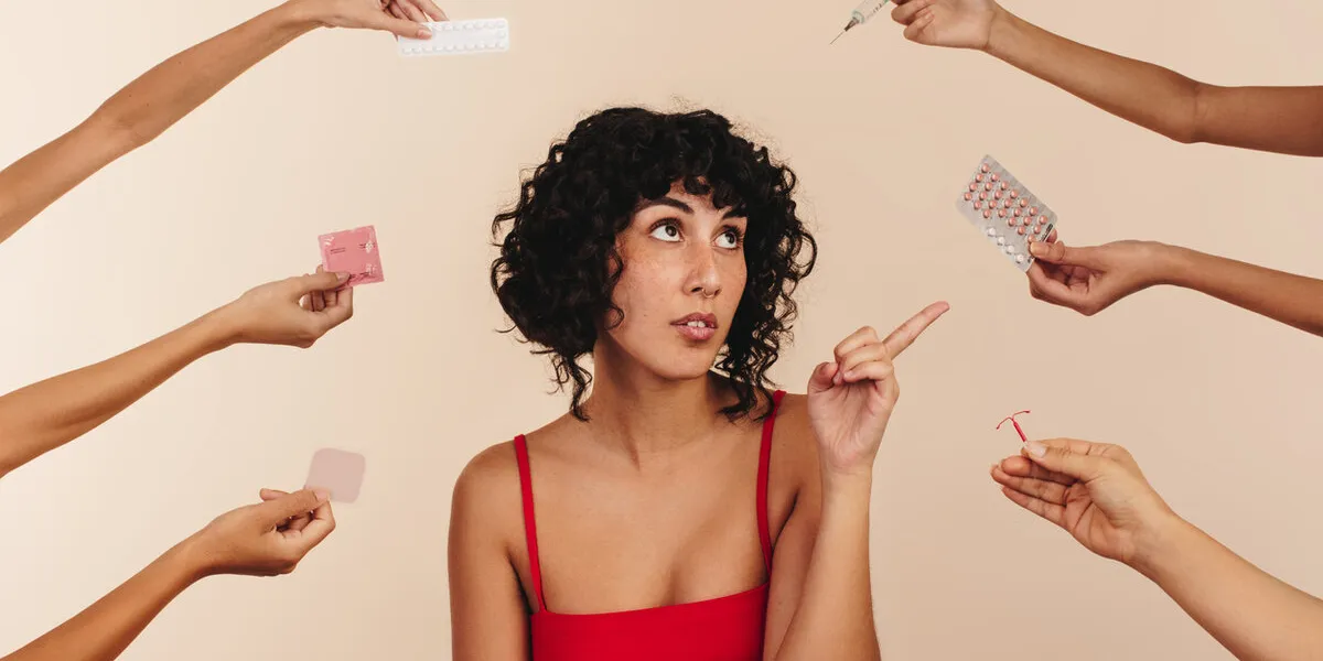 young woman pointing at a pack of pills while surrounded by hands holding different forms of hormonal and non-hormonal contraception modern young woman making choices about her reproductive health young woman pointing at a pack of pills while surrounded by hands holding different forms of hormonal and non-hormonal contraception modern young woman making choices about her reproductive health