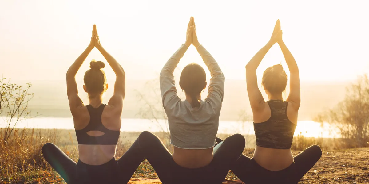rear view of three women meditate at sunset in nature collective yoga classes in outdoor rear view of three women meditate at sunset in nature collective yoga classes in outdoor