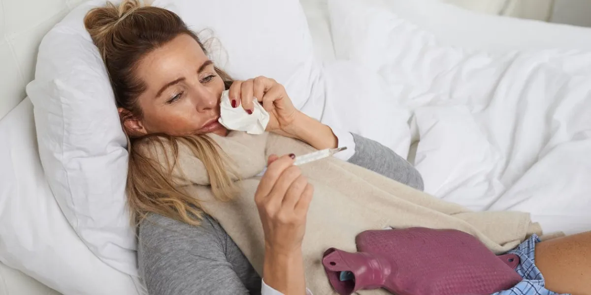 sick woman with a miserable expression taking her temperature as she lies in bed suffering from a seasonal cold and flu trying to keep warm sick woman with a miserable expression taking her temperature as she lies in bed suffering from a seasonal cold and flu trying to keep warm