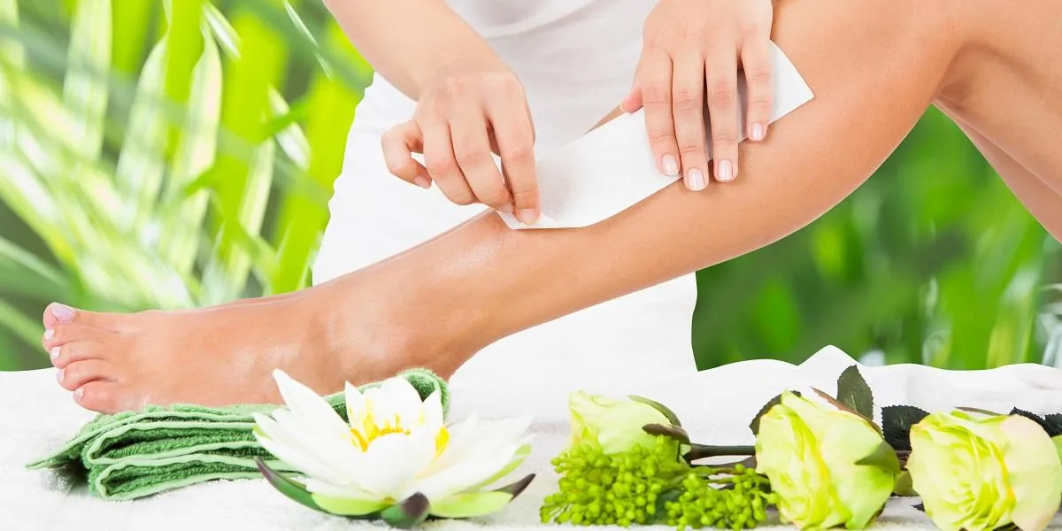 midsection of beautician waxing woman's leg with wax strip at beauty spa