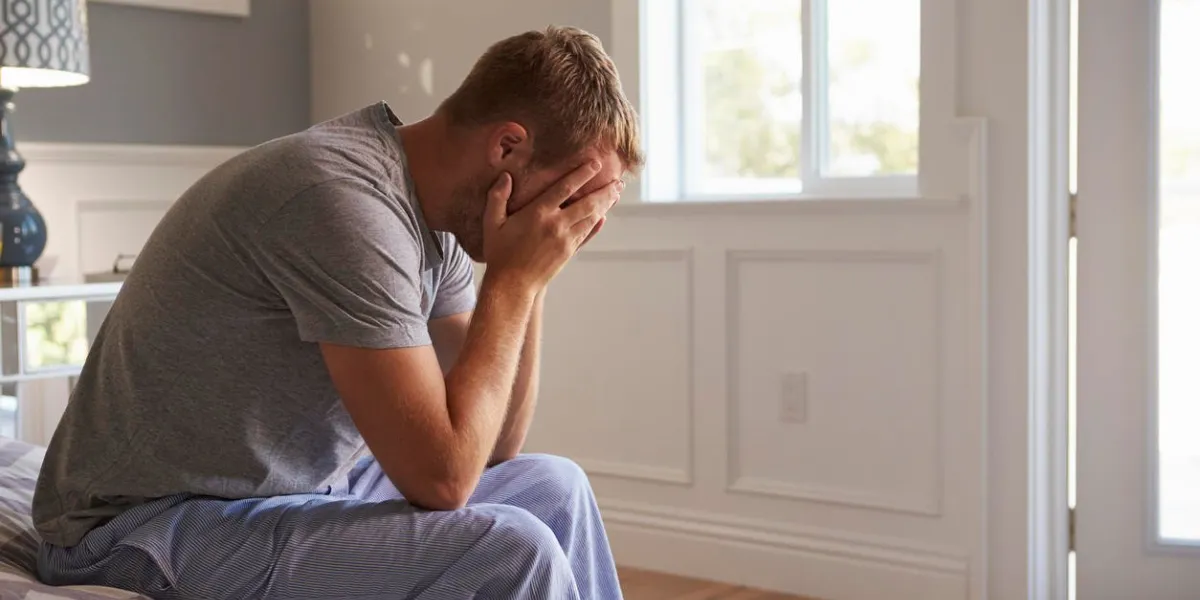 homme portant des pyjamas assis sur le lit avec la tête dans les mains homme portant des pyjamas assis sur le lit avec la tête dans les mains
