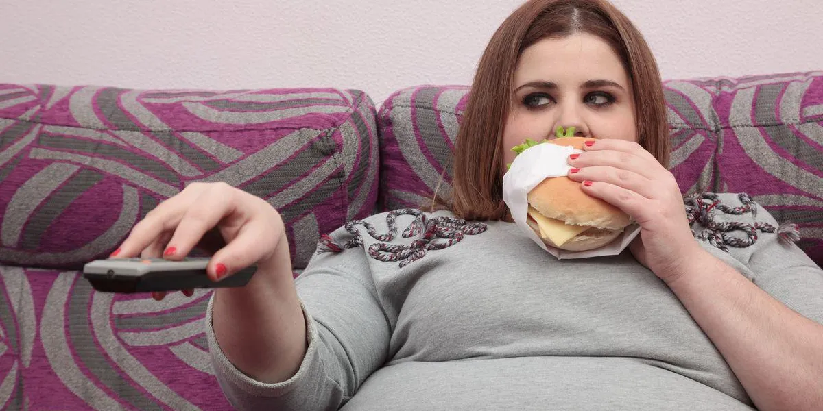 femme avec un excès de poids manger un hamburger et regarder la télévision