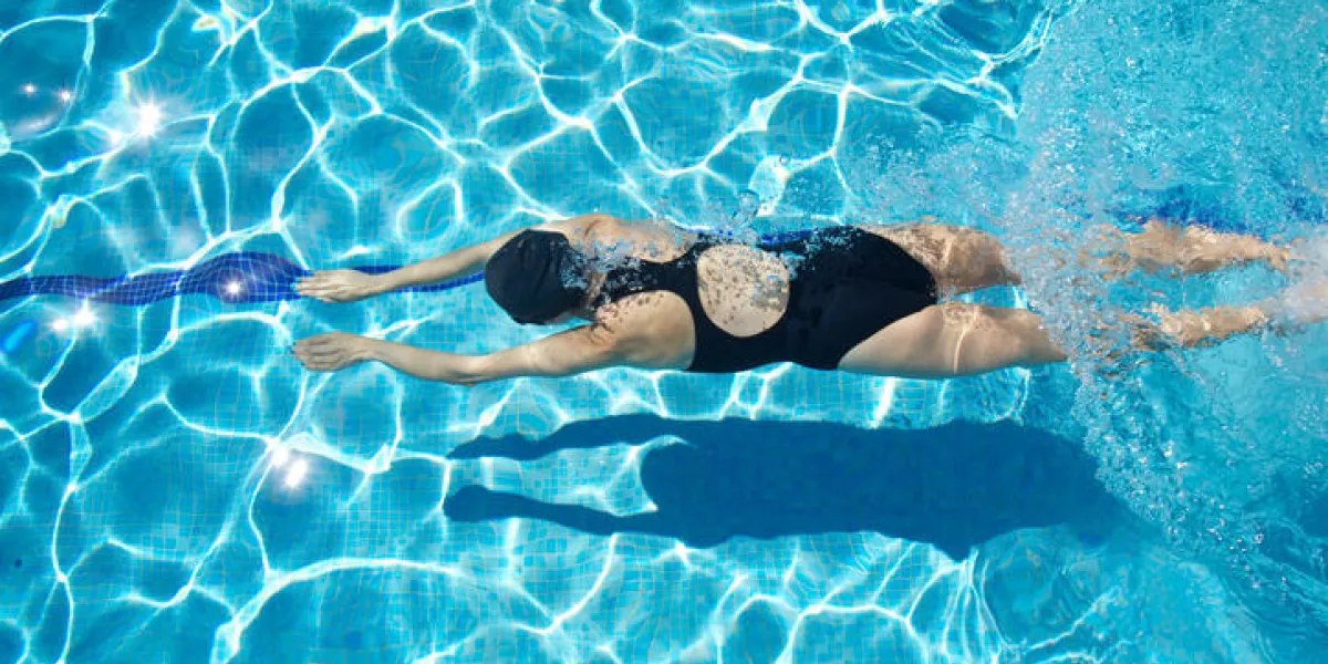 femme de sport avec maillot de bain noir et capuchon nager et plonger dans une piscine d'eau reflétant bleu