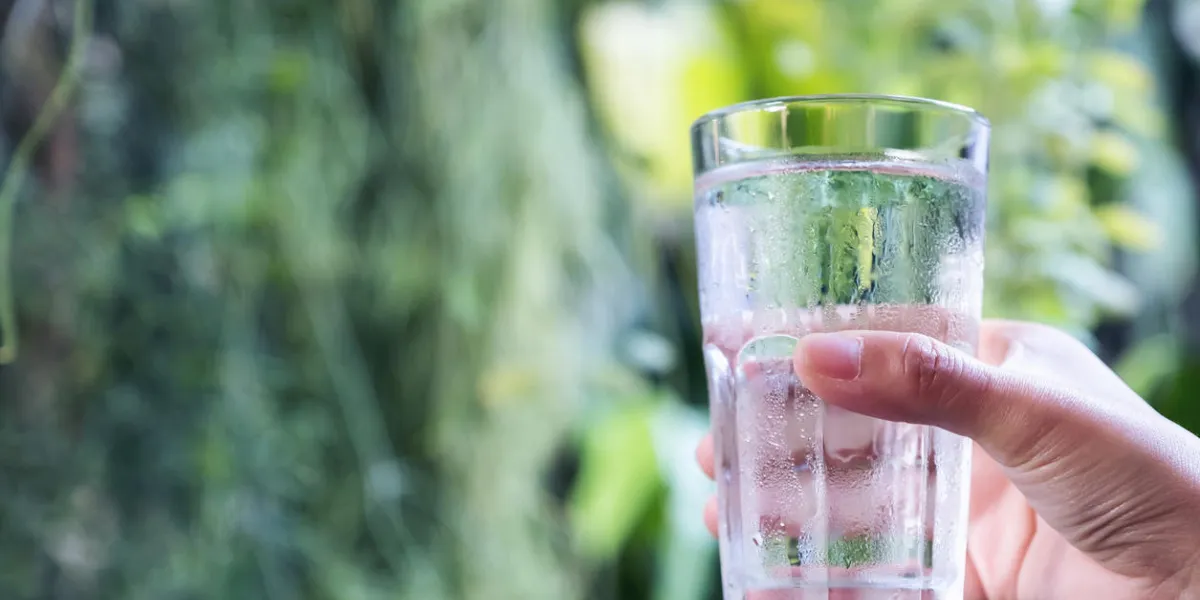closeup image of a hand holding and raising a glass of cold water with green nature background