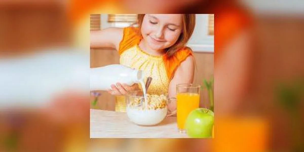 heureuse petite fille verse le lait dans des flocons de céréales pour le petit déjeuner