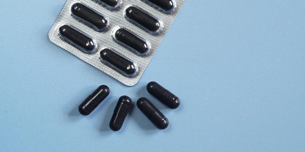 capsules médicales avec du charbon activé sur un fond bleu, vue de dessus