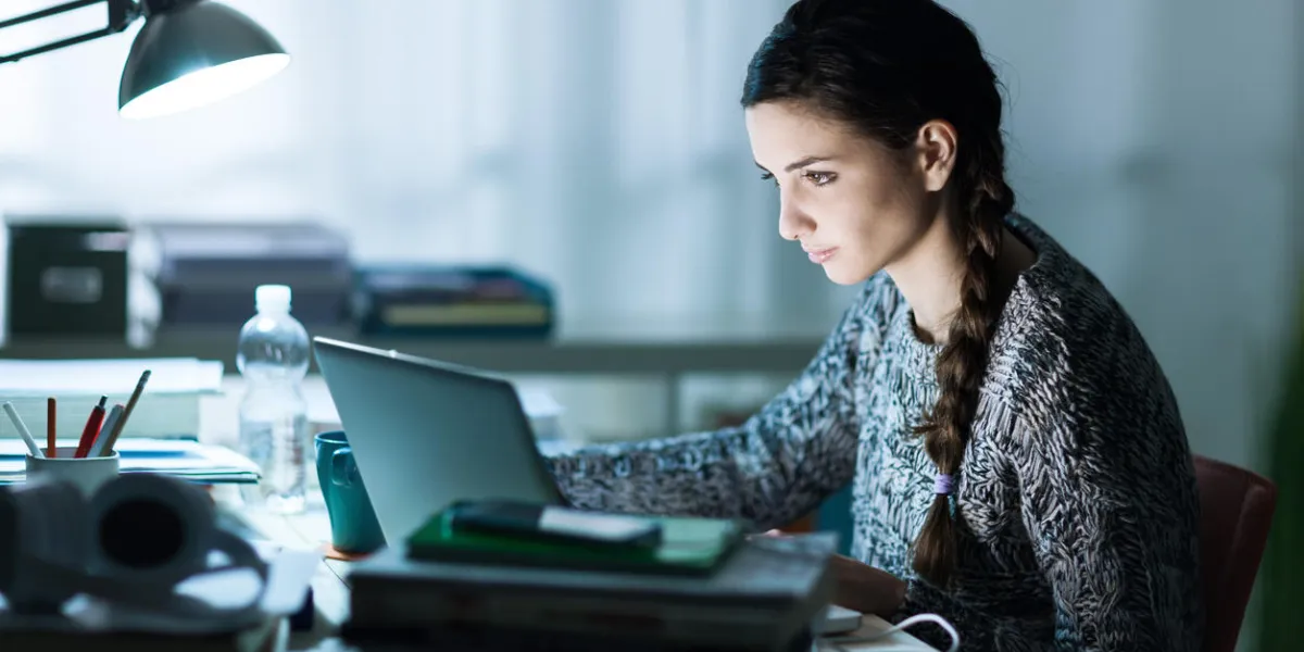 pretty young student sitting at desk and doing her homework, she is connecting to the internet with a laptop pretty young student sitting at desk and doing her homework, she is connecting to the internet with a laptop