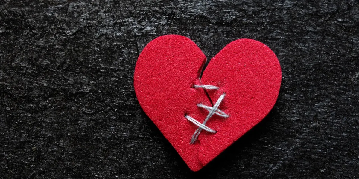 red broken heart with thread stitches on dark background red broken heart with thread stitches on dark background