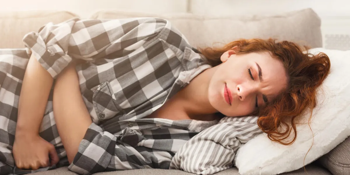 young redhead woman suffering from stomachache lying on couch at home, copy space