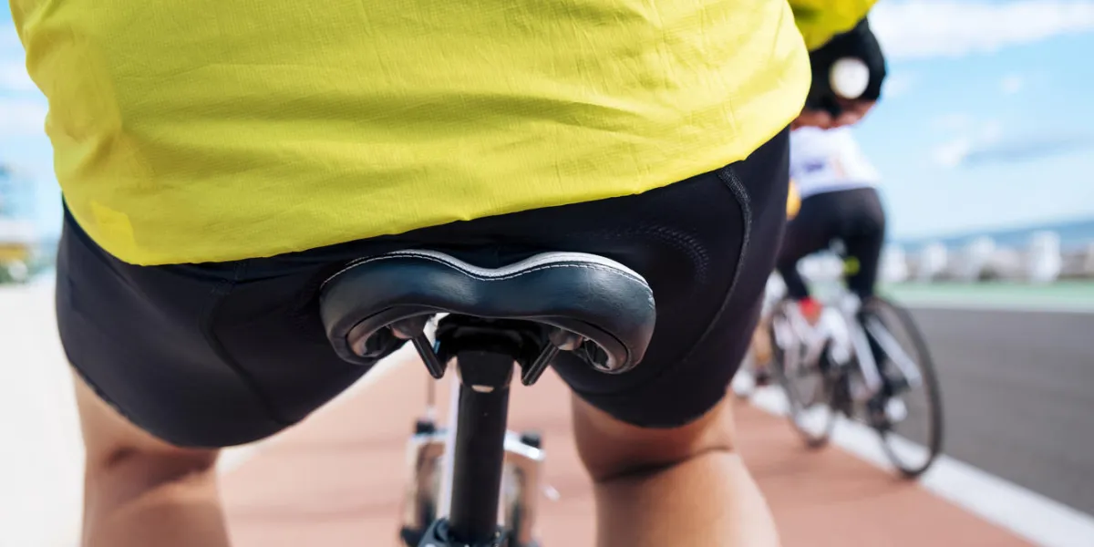 closeup of a young caucasian man wearing sport clothes seen from behind riding his bicycle by a bike lane next to the ocean