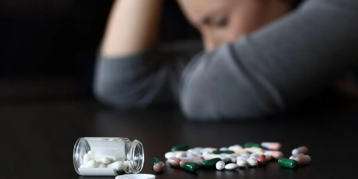 close up of a depressed woman beside a lot of pills on a table on a dark background