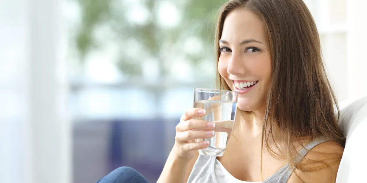 fille de l'eau potable assis sur un canapé à la maison et en regardant la caméra