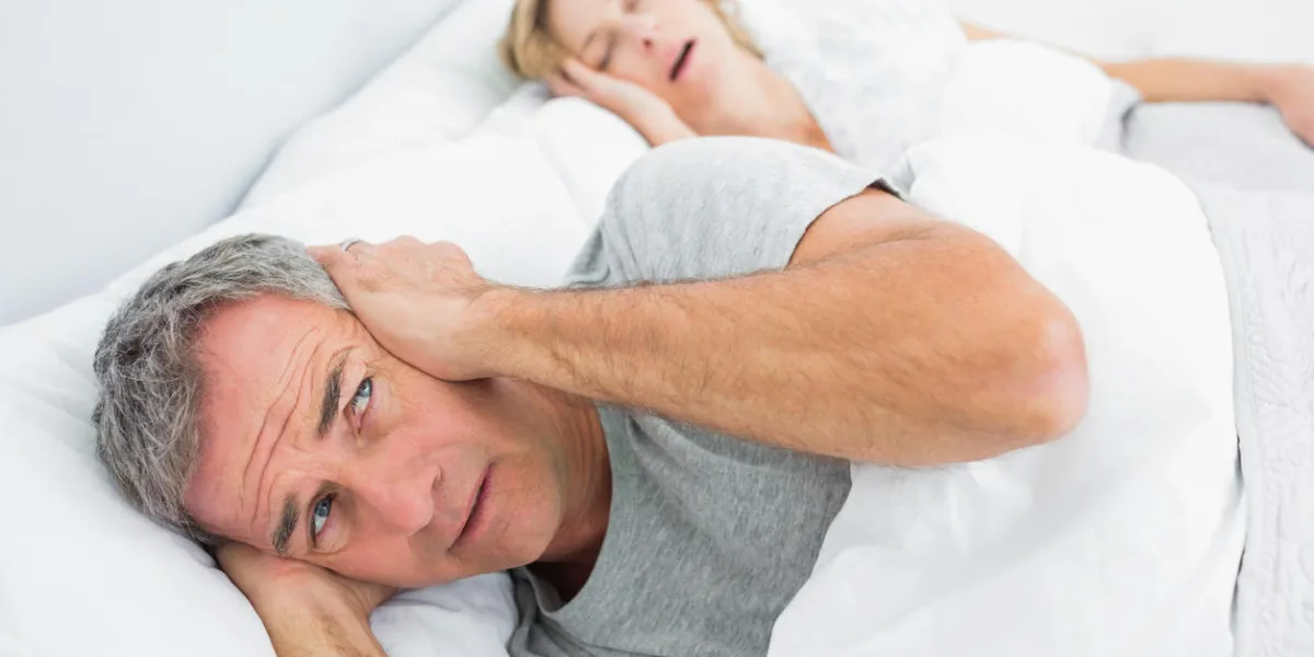 fed up man blocking his ears from noise of wife snoring at home in bedroom