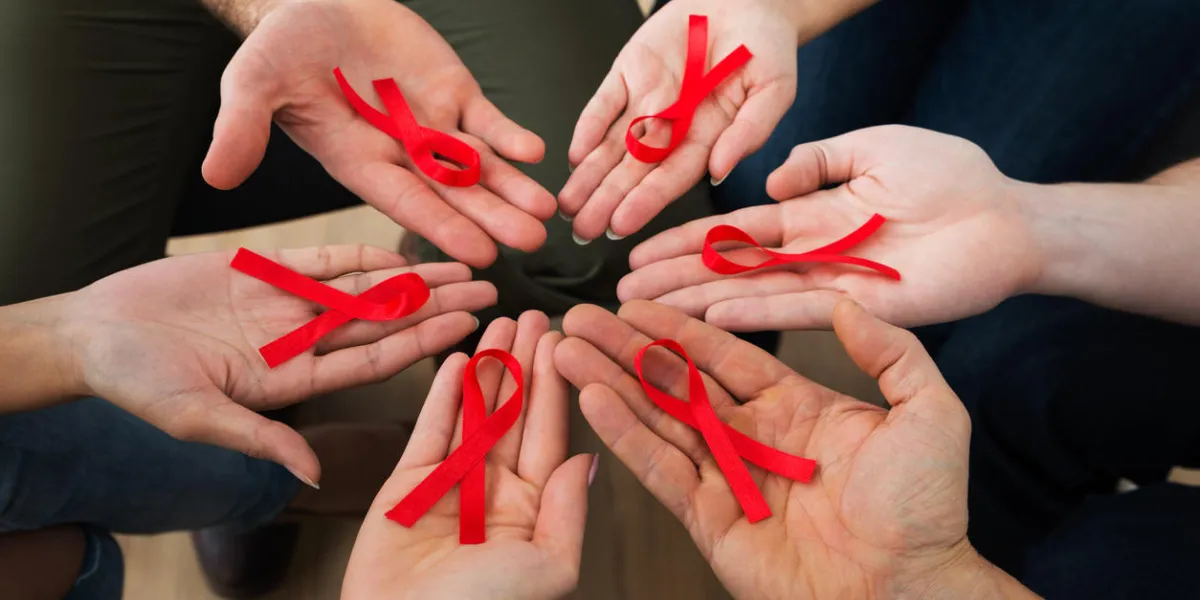 close-up of people holding red aids awareness ribbon on palm close-up of people holding red aids awareness ribbon on palm