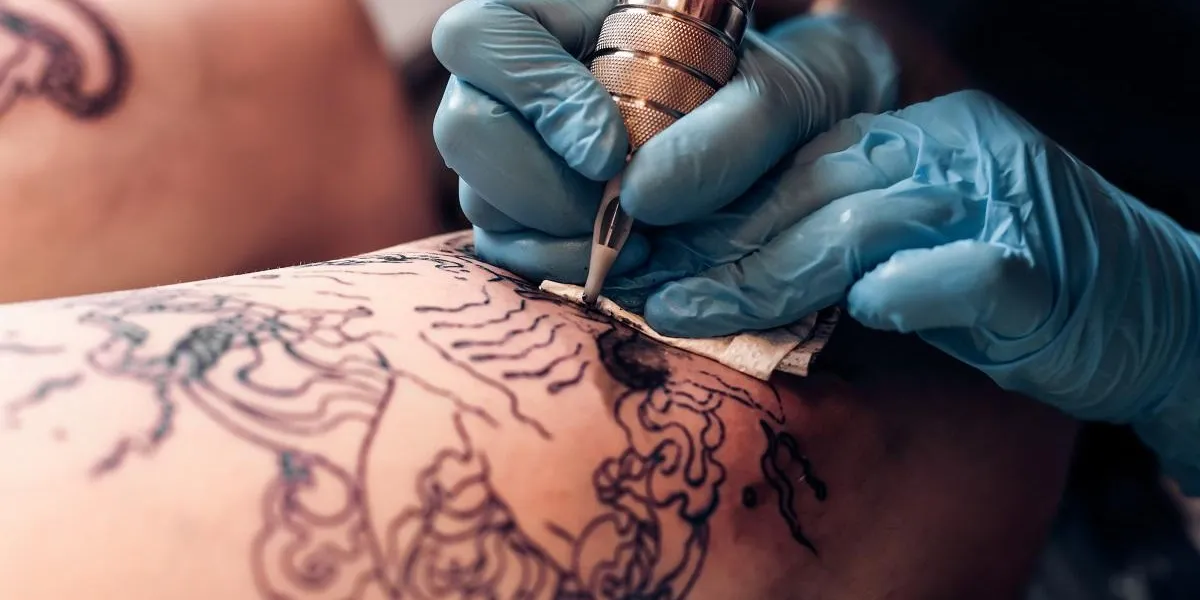 closeup tattoo artist fill circuit tattoo in a professional salon leg with a pattern and black paint master works in black sterile gloves