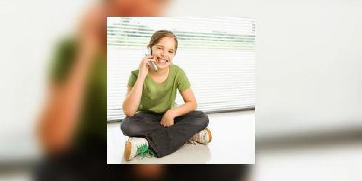 caucasienne préadolescente, assis sur le plancher, parler sur téléphone portable et souriant au spectateur