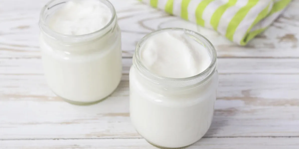 homemade yogurt in glass jar with green dishcloth on wooden table